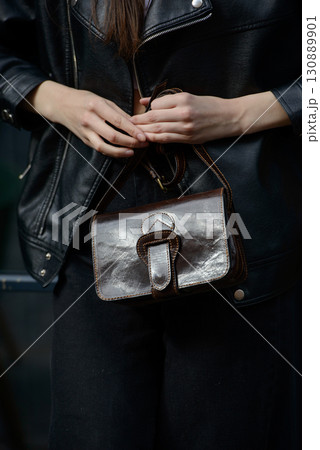 A stylish model in a black leather jacket showcases a unique black leather cross-body bag with a glossy sheen and a front flap pocket A stylish model in a black leather jacket showcases a unique black leather cross-body bag with a glossy sheen and a front flap pocket 130889901