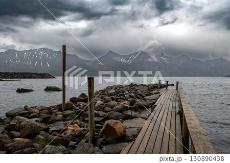 Wooden Pier At Rainy Weather In Fjord With Snowy Mountains On Senja Island In Mefjordvaer In Norway Wooden Pier At Rainy Weather In Fjord With Snowy Mountains On Senja Island In Mefjordvaer In Norway 130890438