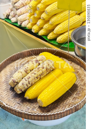 Steamed and grilled corn cobs presented on a woven basket, drizzled with butter, capture the essence of street food with their vibrant, tempting colors and rustic charm. Vertical format 130890835