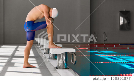 Focused swimmer preparing on starting block before competitive pool race 130891877