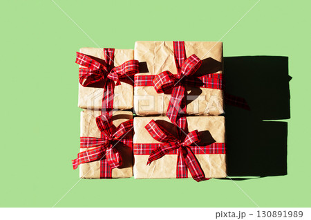 Four gift boxes wrapped in brown paper with red plaid ribbon on green background for Christmas holiday. Four gift boxes wrapped in brown paper with red plaid ribbon on green background for Christmas holiday. 130891989
