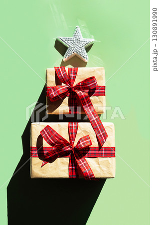 Two gift boxes wrapped in craft paper with red plaid ribbon, topped with star, simulating Christmas tree. Two gift boxes wrapped in craft paper with red plaid ribbon, topped with star, simulating Christmas tree. 130891990