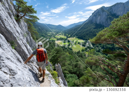 Hiker walking on a cliff edge enjoying scenic valley view 130892338