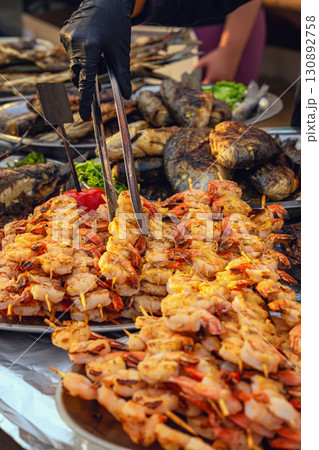 Grilled Shrimp Skewers. Description: Skewers of grilled shrimp being served with tongs at seafood stall. Concept of grilled seafood, barbecue, outdoor food festival 130892758