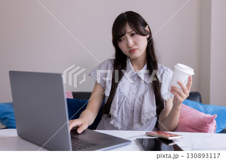 リビングで悩んだ表情を浮かべながらPC作業をする日本人女性 リビングで悩んだ表情を浮かべながらPC作業をする日本人女性 130893117