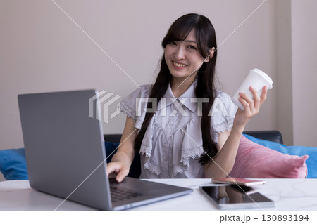 リビングでマグカップを手にPC作業をする笑顔の日本人女性 リビングでマグカップを手にPC作業をする笑顔の日本人女性 130893194