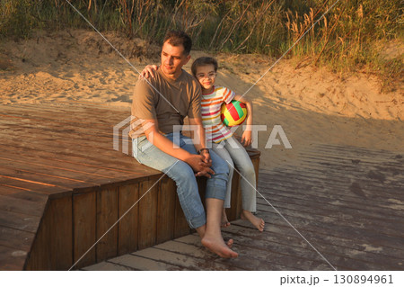 Daughter 8 year old tenderly hugs dad sits on beach Daughter 8 year old tenderly hugs dad sits on beach 130894961