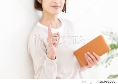 長財布を持って人差し指を立てるカジュアルのミドル女性 130895333