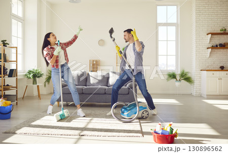 Funny couple cleaning home together having fun, dancing at home while housekeeping work 130896562