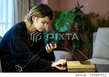 荷物の前でスマホを操作するZ世代の男性 130897012