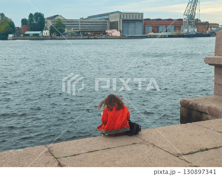 lonely girl sits on the riverbank in the city lonely girl sits on the riverbank in the city 130897341