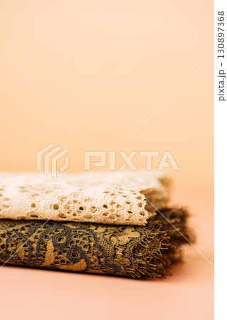 Two folded lace fabrics on peach background, vertical 130897368