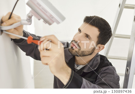 Serious man working in security company, screwing CCTV camera on wall installing surveillance system Serious man working in security company, screwing CCTV camera on wall installing surveillance system 130897436