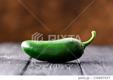 Single green jalapeno hot pepper on rustic wooden table Single green jalapeno hot pepper on rustic wooden table 130897437