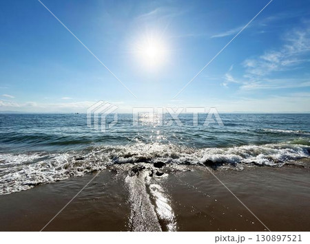 砂浜に打ち寄せる波と海面に反射する太陽光 130897521