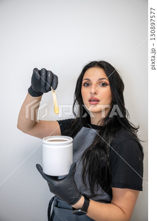 Beautician woman in black gloves holding jar of sugaring paste for hair removal procedure 130897577