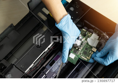 A technician is checking the printer's motherboard circuit board. A technician is checking the printer's motherboard circuit board. 130897717