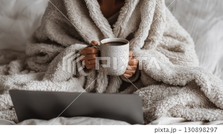 person wrapped in a soft beige blanket, holding a ceramic mug 130898297