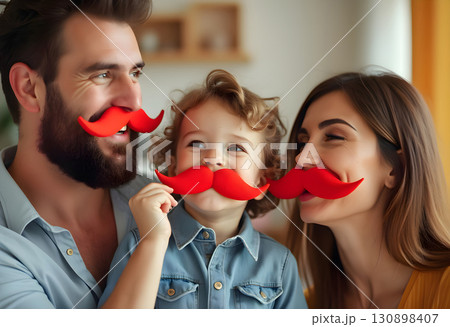 Family enjoying playful moment at home with red mustache props during fun activity 130898407