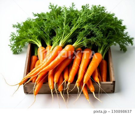 Freshly harvested carrots with green tops displayed in a rustic wooden crate on a light background 130898637