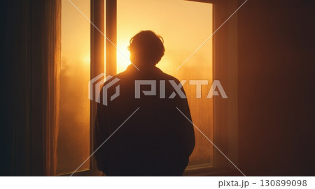 Silhouette of a Person Watching Sunrise Through a Glass Window 130899098