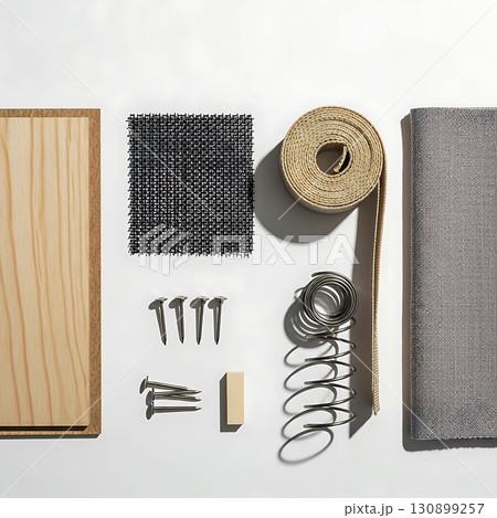 Wooden panel, nails, mesh square, coiled spring, fabric rolls, small block and nail roll neatly arranged on a surface. Shadows cast by overhead light enhance the textures 130899257