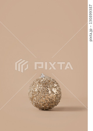 Christmas golden shiny bauble on beige background. Xmas greeting card. New Year minimal concept. Mocha Mousse. Mocha Mousse. Vertical format. Christmas golden shiny bauble on beige background. Xmas greeting card. New Year minimal concept. Mocha Mousse. Mocha Mousse. Vertical format. 130899387