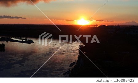 Po River sunset glowing with warm hues, industrial chimneys and mountain silhouettes framing scenic landscape of Cremona, Lombardy, Italy Po River sunset glowing with warm hues, industrial chimneys and mountain silhouettes framing scenic landscape of Cremona, Lombardy, Italy 130899422