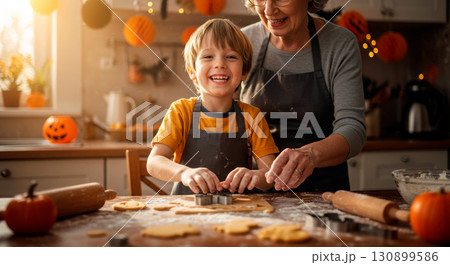 Joyful grandmother and grandson baking Halloween cookies together in a kitchen 130899586