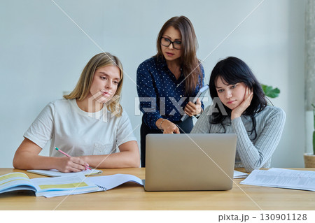 Two university student girls with female teacher mentor study while sitting at desk 130901128