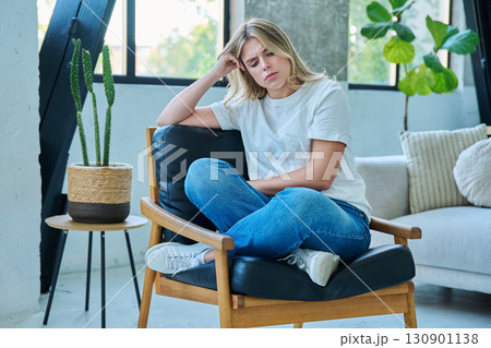 Unhappy upset tired young woman sitting in chair at home Unhappy upset tired young woman sitting in chair at home 130901138
