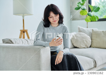 Smiling young woman with smartphone sitting at home on sofa 130901162