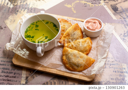 A bowl of broth and several small chebureki with sauce 130901263