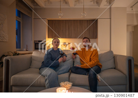 Romantic resting couple watching TV wiith wine glasses and popcorn in softly lit lounge at home 130901487