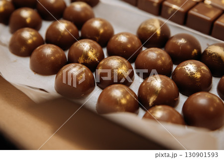 Luxury handmade chocolate bonbons with golden decor arranged in rows on parchment paper 130901593