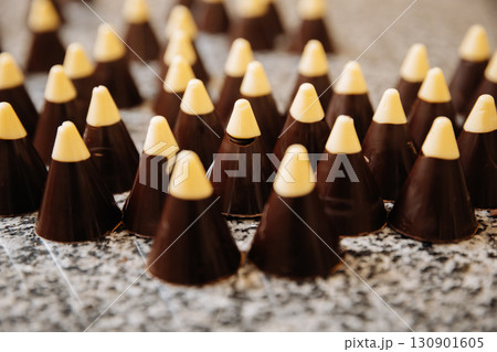 Chocolate cone candies with white tips arranged on granite surface in confectionery workshop 130901605