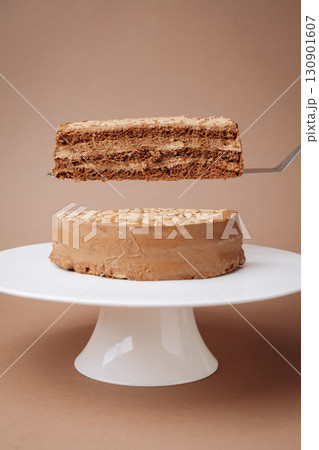Slice of layered chocolate cake lifted on spatula over whole cake on stand Slice of layered chocolate cake lifted on spatula over whole cake on stand 130901607