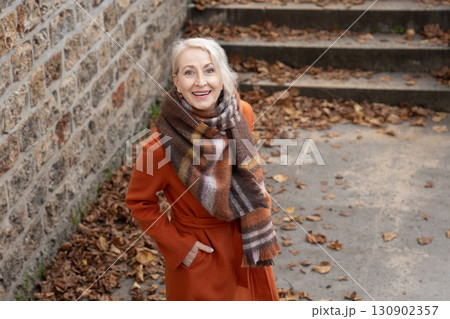 Gray-haired woman of sixty years old in a orange coat and a terracotta scarf 130902357