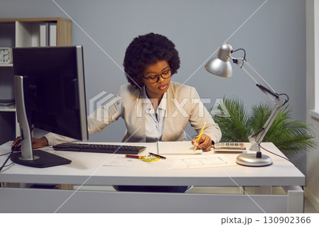 Focused businesswoman making notes on paper while working on laptop 130902366