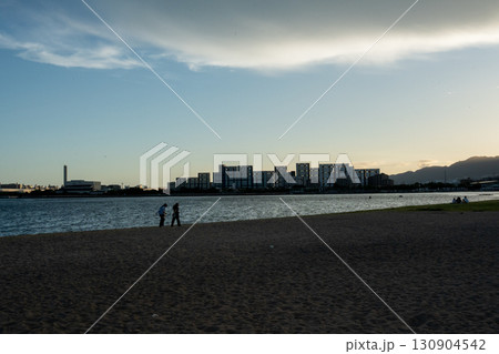 夕暮れの海岸沿いを歩くカップル 130904542