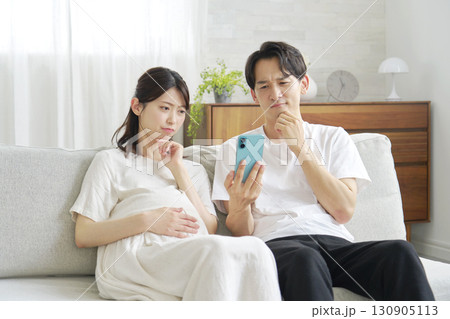 スマートフォンを持って考える妊娠中の妻と夫 130905113