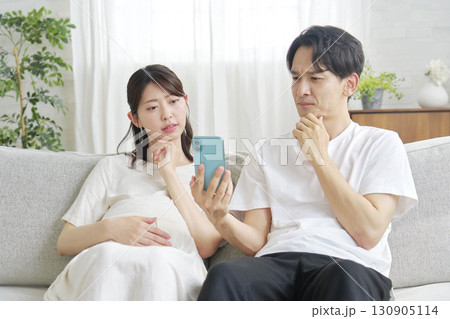 スマートフォンを持って考える妊娠中の妻と夫 130905114