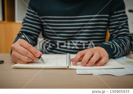 hand holding pen and wtiting notebook at home office hand holding pen and wtiting notebook at home office 130905835
