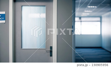 A closed, gray hospital or office door with a vertical glass window is seen in a clean, empty hallway. 130905956