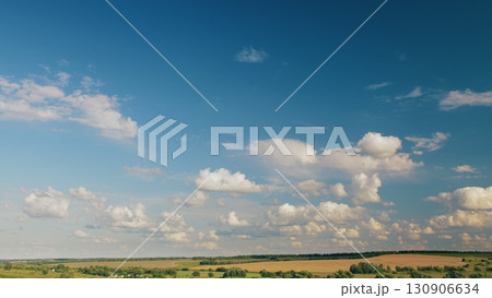 A Vast Open Sky with Fluffy Clouds Gracefully Draped Over a Lush Green Landscape 130906634