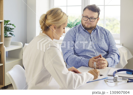 Physician writing notes while counseling obese patient during health consultation Physician writing notes while counseling obese patient during health consultation 130907004