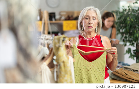 Attentive mature woman choosing something for summer in clothing store Attentive mature woman choosing something for summer in clothing store 130907123