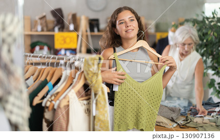 Young woman chooses a set of clothes for the summer. Visitor to the boutique examines new summer collection of clothes Young woman chooses a set of clothes for the summer. Visitor to the boutique examines new summer collection of clothes 130907136