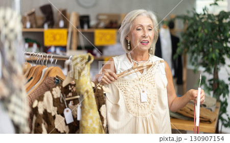 Positive mature woman choosing something for summer in clothing store 130907154