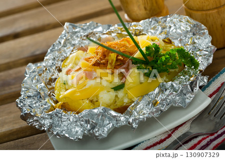 Baked in foil potatoes with filling of bacon, cheese and fried onion Baked in foil potatoes with filling of bacon, cheese and fried onion 130907329